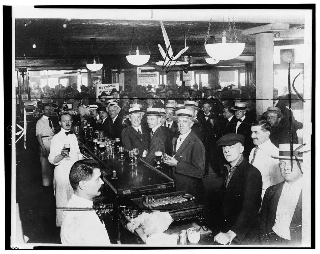 Photo of men gathered around the bar. Shot in early 1920s.