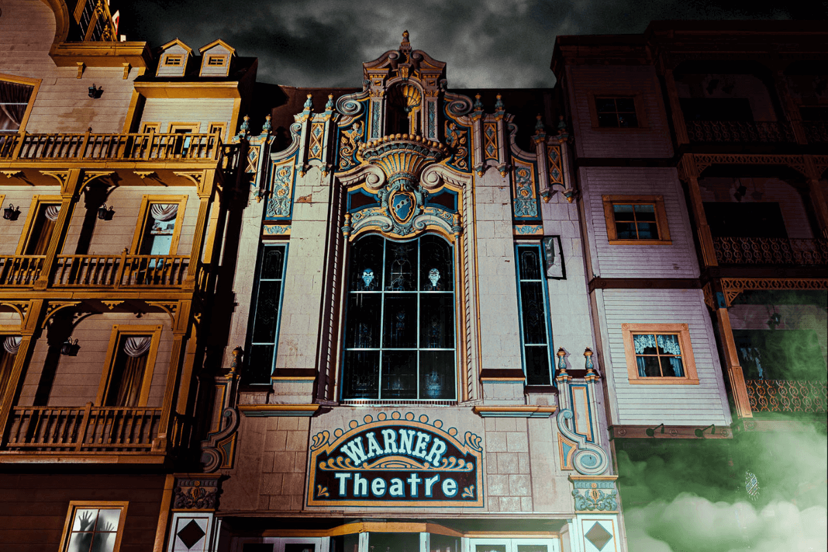 Historic stone multi level building with ornate design. Gold colored porches on multiple levels and Warner Theatre adorning the front in white, black and gold.